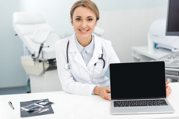 超音波スキャン付きのプロの笑顔の女性医師は、空白の画面でラップトップを示す - 写真・画像