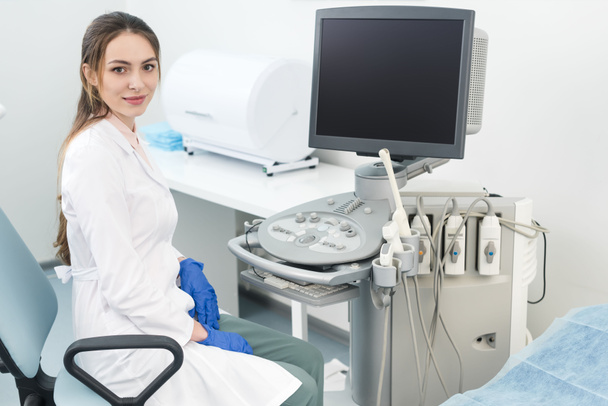 joven médico feliz trabajando con escáner de ultrasonido con pantalla en blanco en la clínica
 - Foto, imagen