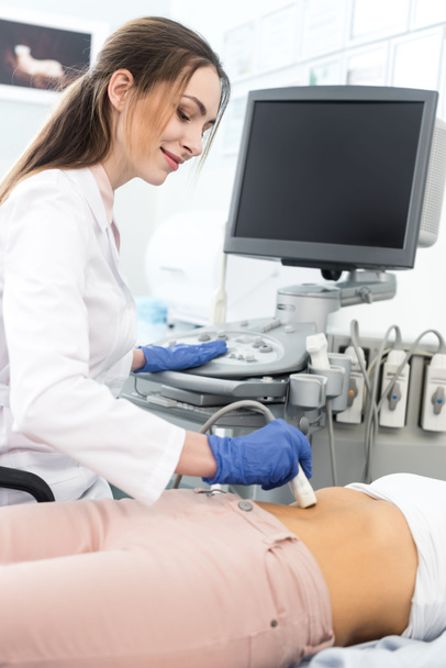 Genç doktor, klinikte ultrason taraması yapılan bir kadının midesini inceliyor.  - Fotoğraf, Görsel