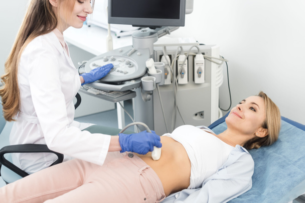 sonriente hermoso doctor examinando estómago de mujer paciente con ultrasonido escanear en clínica
  - Foto, imagen