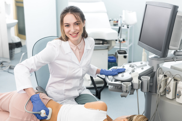 Gülümseyen genç doktor, klinikte ultrason taraması yapılan bayanın böbreğini inceliyor.   - Fotoğraf, Görsel