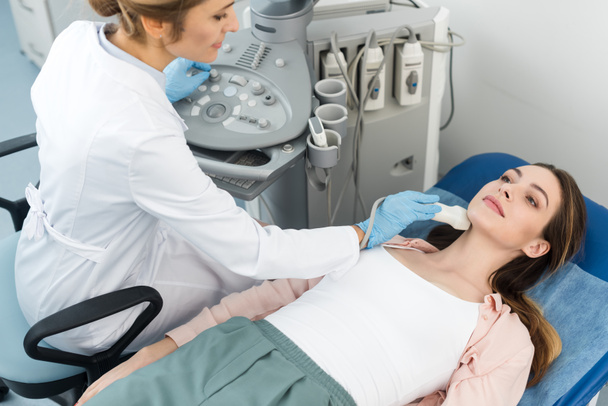 лікар вивчає щитоподібну залозу молодої жінки з ультразвуковим скануванням у клініці
 - Фото, зображення