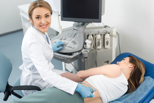 Lächelnder Arzt untersucht Niere einer Patientin mit Ultraschall in Klinik   - Foto, Bild