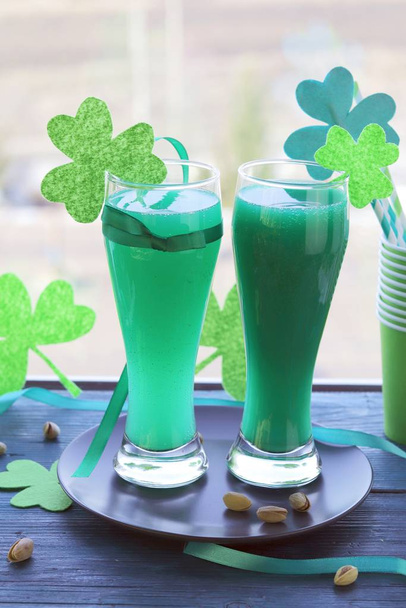Den svatého Patrika, sklenice se zeleným nápojem, koktejlové trubice s dekorativním shamrockem, jetel na dřevěném povrchu na okenním pozadí, příprava na párty - Fotografie, Obrázek