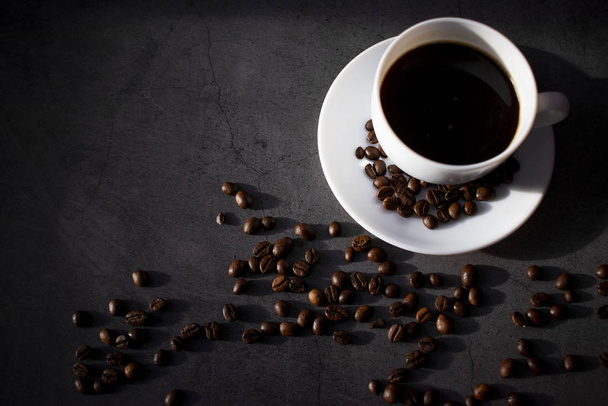 Біла чашка з тарілкою та кавовими зернами, ароматна, гаряча кава на темній плоскій поверхні
 - Фото, зображення