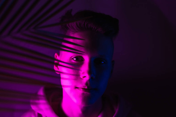 Egy fiatal fickó tenyérlevéllel neonfényben a kamerába néz. Trend fotó egy tinédzser - Fotó, kép