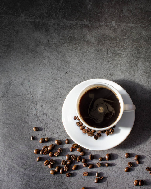Біла чашка з тарілкою та кавовими зернами, ароматна, гаряча кава на темній плоскій поверхні
 - Фото, зображення