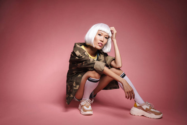 Image of young asian girl wearing white wig sitting and looking  - Foto, afbeelding