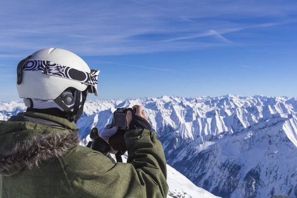 Narciarz w pomarańczowych okularach narciarskich w białym hełmie robi sesję zdjęciową na szczycie Alp. Na tle gór. Widok z bliska. - Zdjęcie, obraz