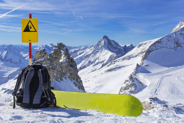 Snowboard εξοπλισμός, ένα σακίδιο και μια snowboard βρίσκονται στην άκρη ενός γκρεμού στο φόντο ενός πανοράματος των βουνών. - Φωτογραφία, εικόνα