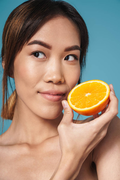 Portrait of half-naked asian woman holding orange and looking aside - Foto, Bild