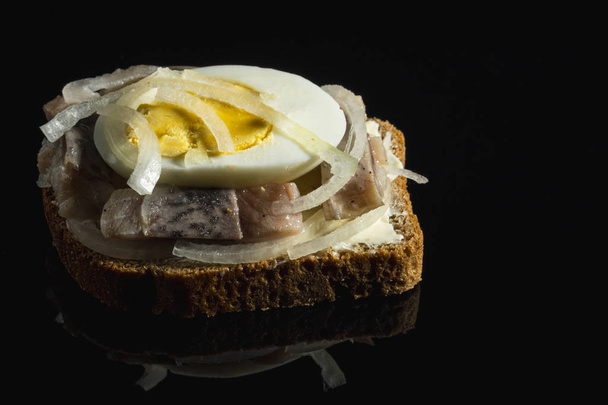 Sandwich with herring, onions and chicken egg. National Russian cuisine. Black glass background, close up - Photo, Image