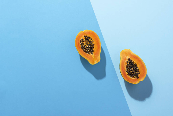 Свежие фрукты папайи разрезаны пополам на голубом фоне. Тропические фрукты
 - Фото, изображение