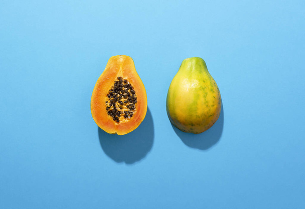 Стиглі плоди папайї, розрізані навпіл на синьому фоні в суворому світлі
 - Фото, зображення