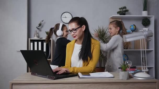 Tired concentrated pretty brunette businesswoman in glasses massaging the temples becouse her noisy playful teen daughters interfering to do her work at home - Video