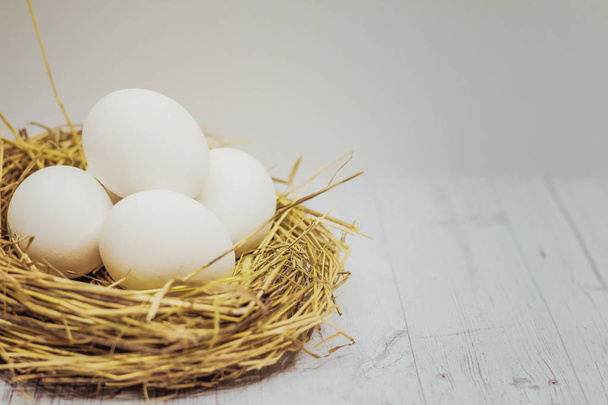 white Easter eggs in a nest on a gray wooden table.  - 写真・画像