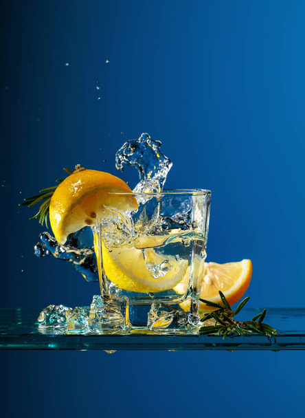 Cóctel gin-tonic con limón y romero sobre una mesa de cristal
. - Foto, imagen