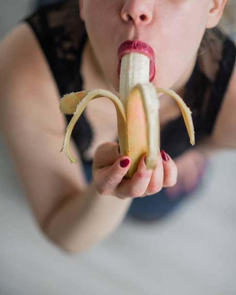 Woman with sensual red lips sucks and licks a banana. Unrecognizable blonde fantasizes about blowjob. Close-up of a female mouth. - Fotó, kép