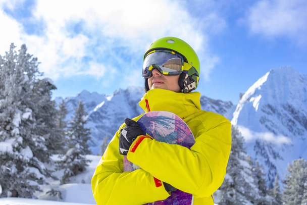 Snowboarder άνθρωπος με γυαλιά σκι σε πράσινο κράνος κάνουν φωτογράφηση στην κορυφή των Άλπεων βουνά. Στο φόντο των βουνών. Κλείσιμο προβολής. - Φωτογραφία, εικόνα