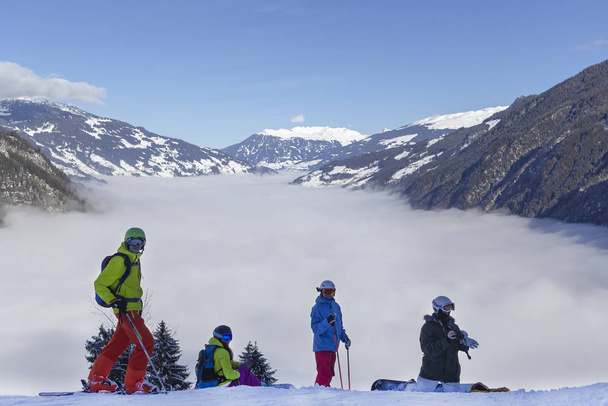 Un río de niebla blanca en las montañas y cuatro personas en frente, snowboarders y esquiadores se están preparando para el descenso..
 - Foto, Imagen