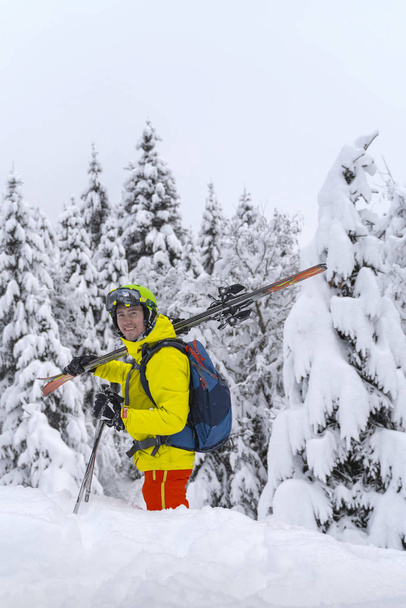 Hombre de color amarillo con mochila azul de esquí estancia con muchos abetos alrededor y suave nieve en polvo. El esquiador de backcountry está en la montaña de los Alpes en Austria
. - Foto, Imagen