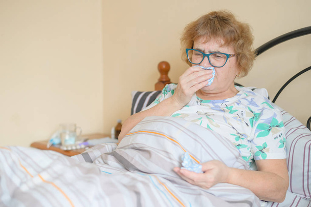 An elderly woman suffers from the flu and runny nose. The pensioner blows her nose in the nasal raft. - Foto, imagen
