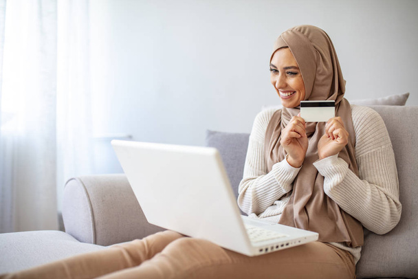Beautiful muslim woman holding credit card. Muslim business woman doing shopping with credit card at home. Cropped shot of attractive female Arabic holding credit card and using laptop for shopping or payment online. - Foto, Bild