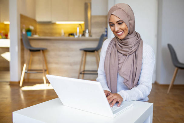 Muslim woman working with computer. Arab Young business woman sitting at her desk at home, working on a laptop computer and drinking coffee or tea. Muslim woman working at a home and using computer. - Photo, Image