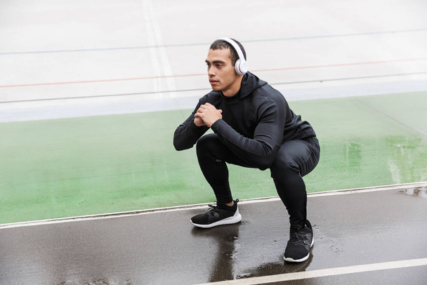 Photo of athletic sportsman doing exercise and using headphones - Fotoğraf, Görsel