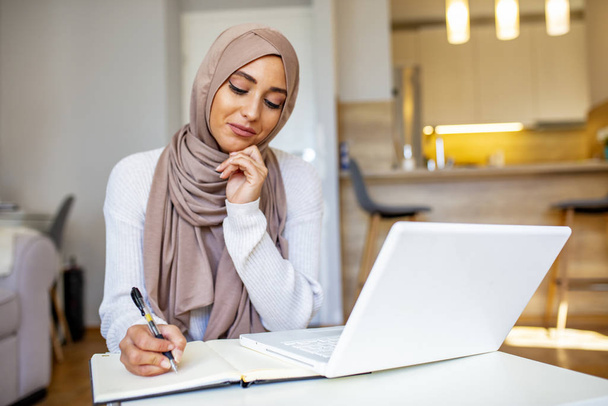 Mujer musulmana desplazándose portátil, trabajando en casa, educación en línea, tecnología. Feliz mujer de negocios musulmana en Hijab en el lugar de trabajo de la oficina. Mujer árabe sonriente trabajando en el ordenador portátil en el proyecto de inicio, espacio de copia
 - Foto, imagen