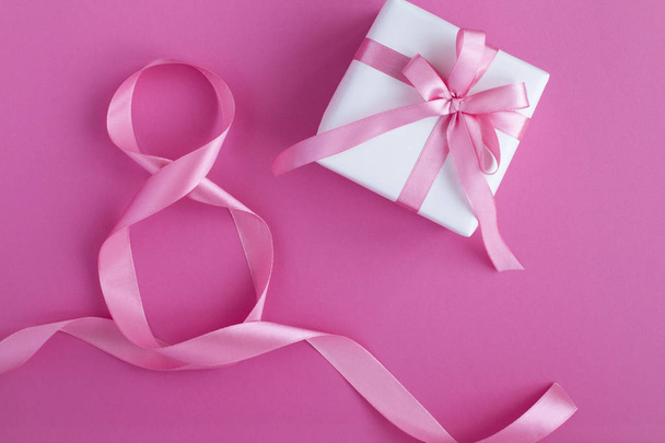 Gift with pink  bow and  pink number eight ribbon on the pink background. Top view. Copy space. - Photo, image