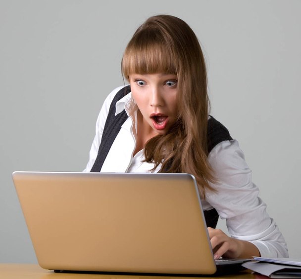 Shocked young girl is looking at a laptop - Foto, imagen