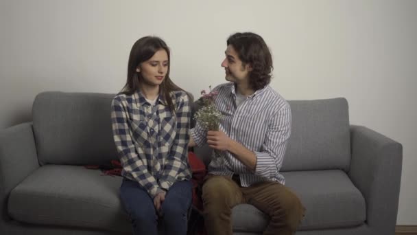 Homem sorridente cobrindo os olhos com a mão para namorada e apresentando buquê na sala de estar
 - Filmagem, Vídeo