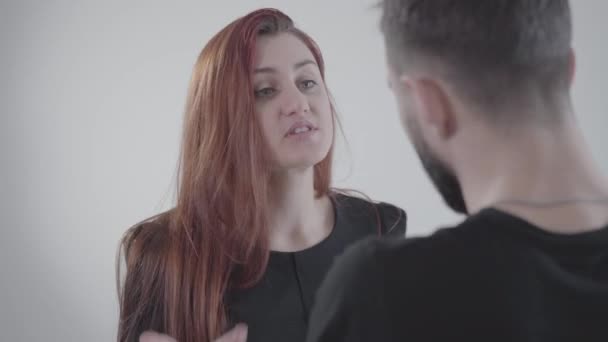 Close-up face of young irritated redhead woman arguing with unrecognizable husband or boyfriend. Two people quarreling at white background. Lifestyle, problem. conflict. - Filmati, video