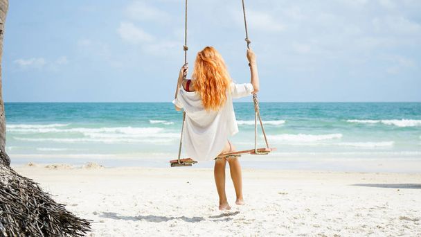 Beach summer vacation tropic palm style portrait of young beautiful girl on beach swing blue sea.Red haired woman swinging on the beach on Phu Quoc island, Vietnam. Happy  on tropical palm tree swing. - Fotoğraf, Görsel