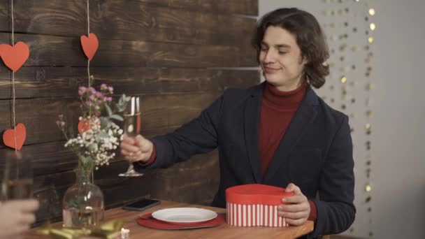 Glimlachende man klinkende glazen champagne en het uitwisselen van valentijnskado 's met vriendin - Video