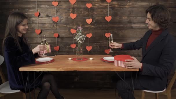 Laughing couple clinking glasses, exchanging valentine presents and kissing during date - Footage, Video