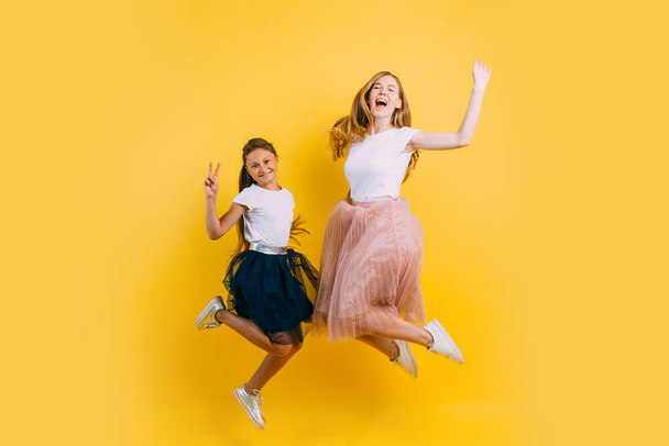 Excited beautiful mom with her daughter on a yellow background B - Фото, изображение