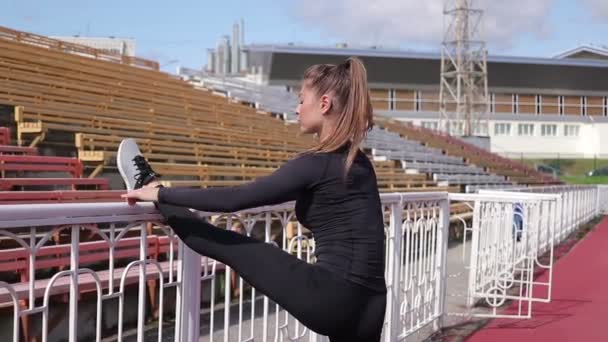 Graceful slim woman warming up at city stadium - Footage, Video