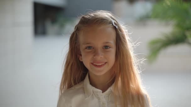 Chica adolescente sonriendo amplia, de pie contra el fondo de la arquitectura
 - Metraje, vídeo