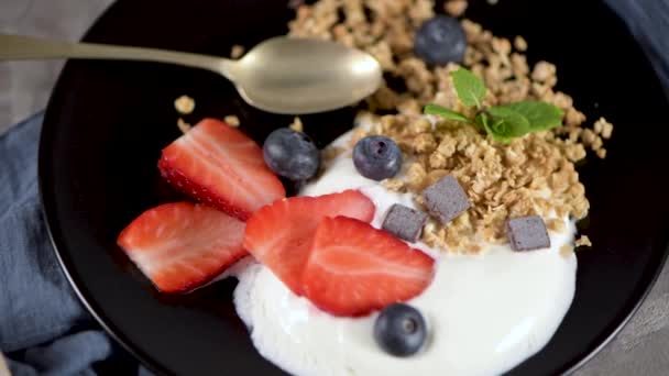 Ripe blueberries and strawberries with yogurt and granola in plate on a light grey background. Healthy Eating. - Filmati, video