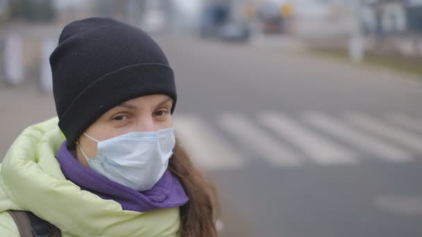 Bescherming tegen het Chinese coronavirus in een Europese stad. Een jonge vrouw op een openbare plaats staat met een medisch masker in Duitsland. Het ontstaan van symptomen van het coronavirus. - Video