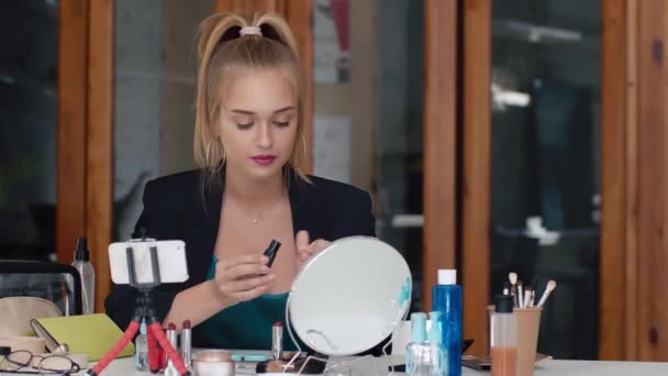 Attractive beauty blogger applying lipstick while happily recording make-up tutorial video for internet - Materiał filmowy, wideo