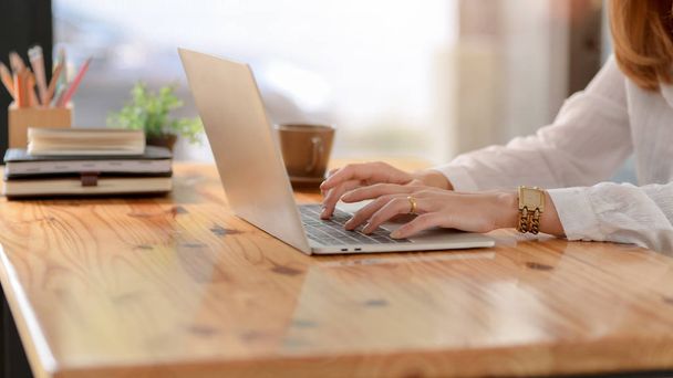 Vista lateral de uma mulher digitando no laptop na mesa de madeira enquanto está sentado no local de trabalho simples
 - Foto, Imagem