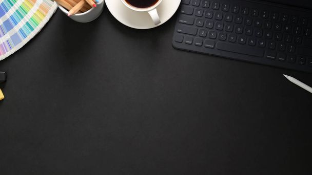 Blick von oben auf den Arbeitsplatz mit drahtloser Tastatur, Malwerkzeugen und Kaffeetasse auf schwarzem Tisch - Foto, Bild