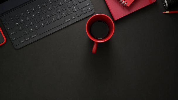 Widok góry stylowego miejsca pracy z klawiaturą bezprzewodową, sprzętem biurowym, przestrzenią do kopiowania i filiżanką czerwonej kawy na czarnym stole  - Zdjęcie, obraz