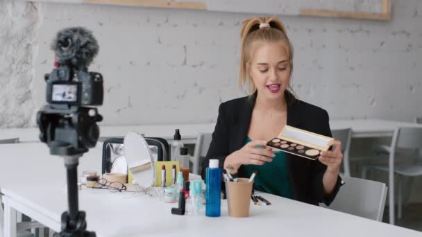 Preciosa bloguera de belleza femenina mostrando alegremente productos cosméticos grabando video tutorial de maquillaje para internet
 - Imágenes, Vídeo