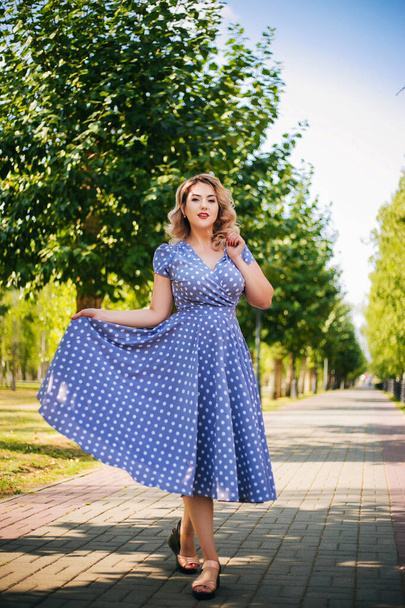 Girl with red lips and a dress in peas on a background of trees in the park. Pin-up model. - Foto, afbeelding