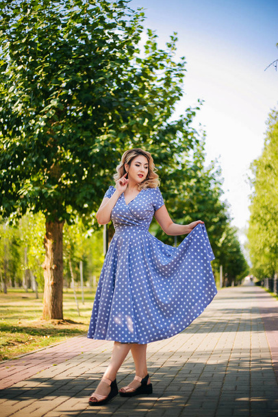 Girl with red lips and a dress in peas on a background of trees in the park. Pin-up model. - Valokuva, kuva