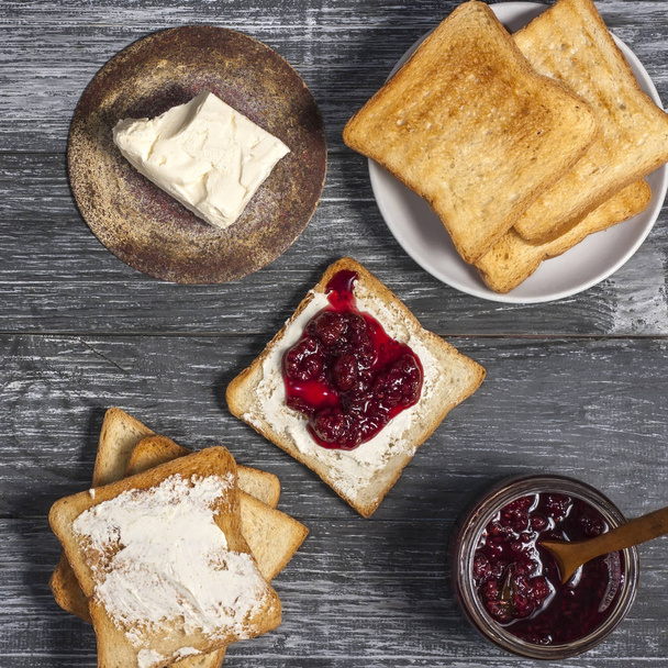 Ingredience na výbornou snídani - opečený chléb s máslem a domácí malinový džem na dřevěném stole. Horní pohled - Fotografie, Obrázek